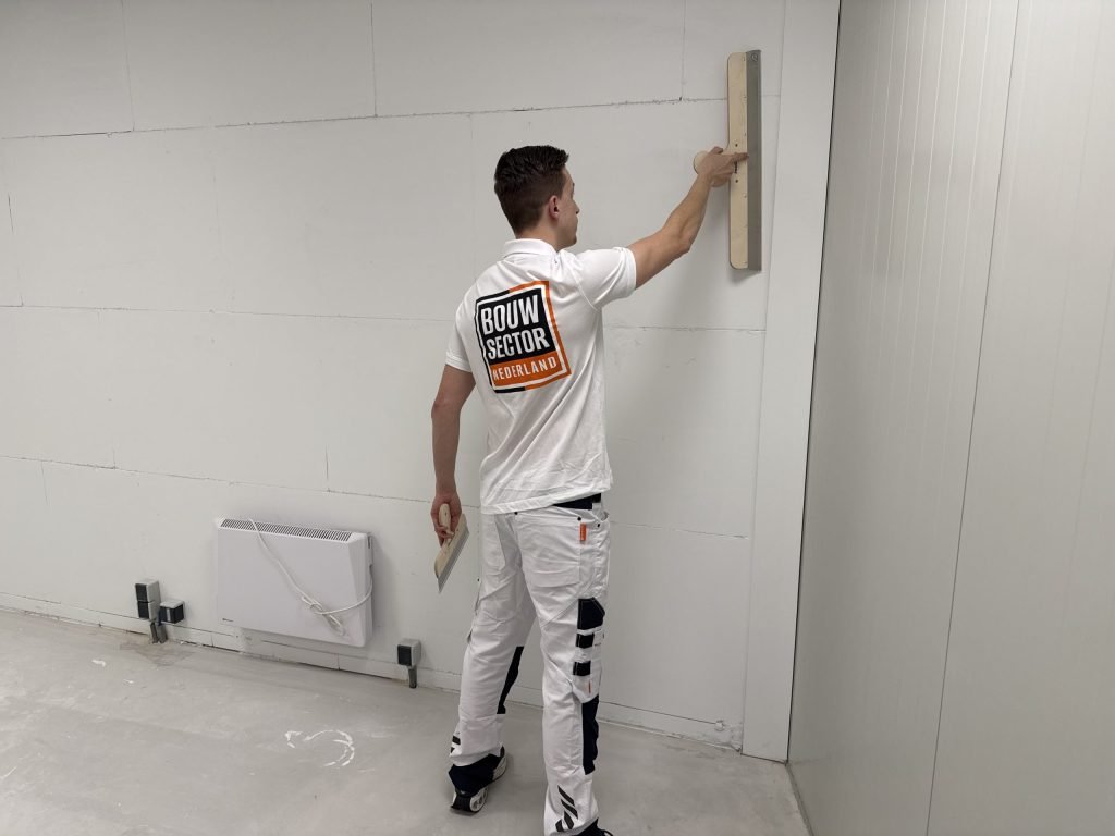 Stukadoor van Bouwsector Nederland trekt met een brede spaan een wand vlak in een lege ruimte met kale vloer