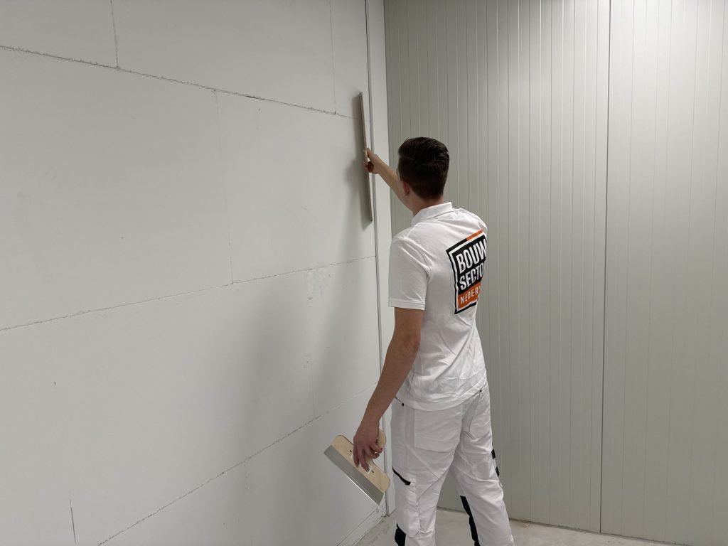 Stukadoor van Bouwsector Nederland schuurt een wand glad met een schuurbord op een steel