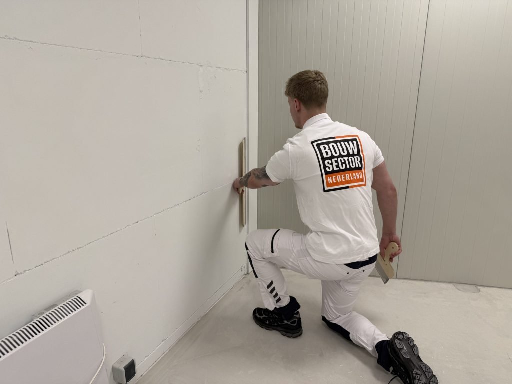 Stukadoor van Bouwsector Nederland werkt geknield met een spaan een naad in de hoek van een wand af